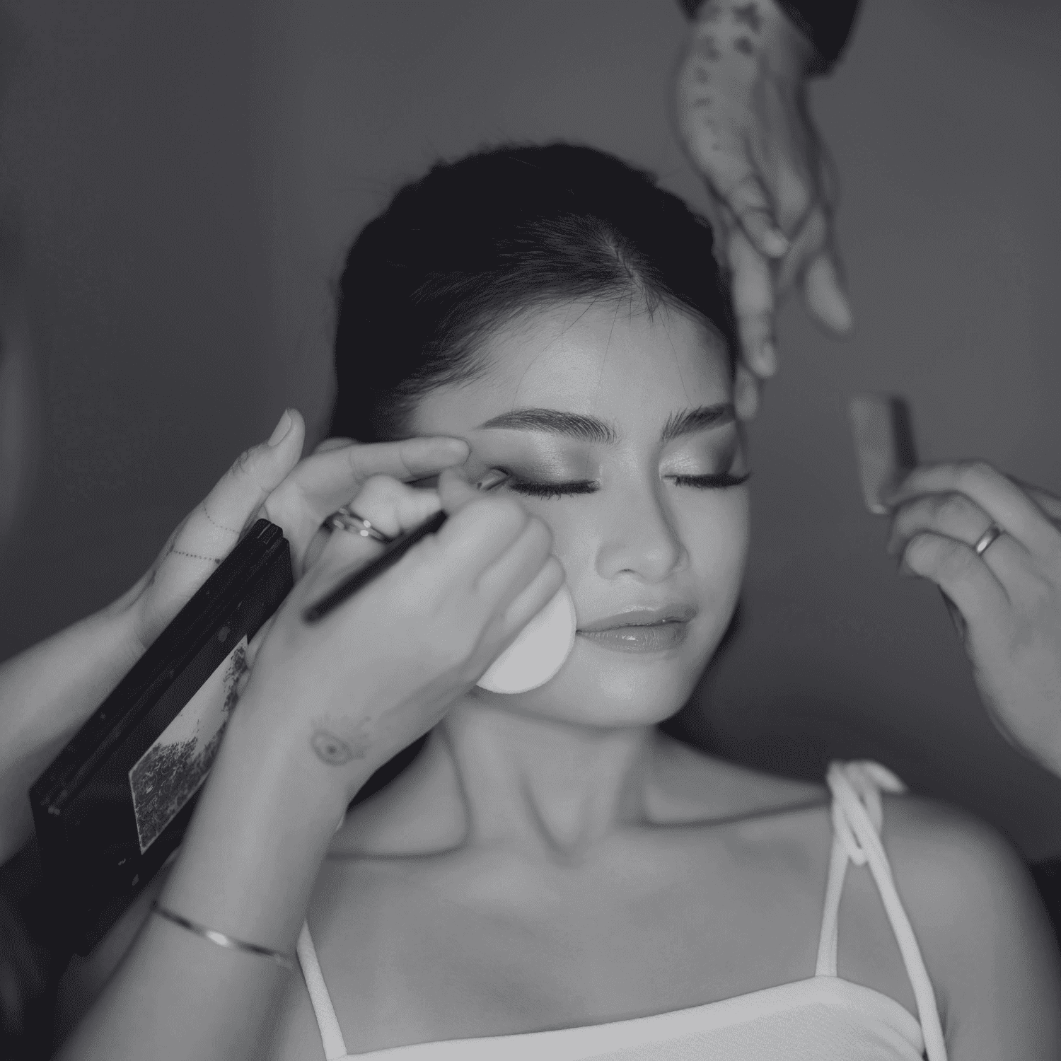 Makeup artist applying cosmetics to a woman’s face with brushes and sponges.